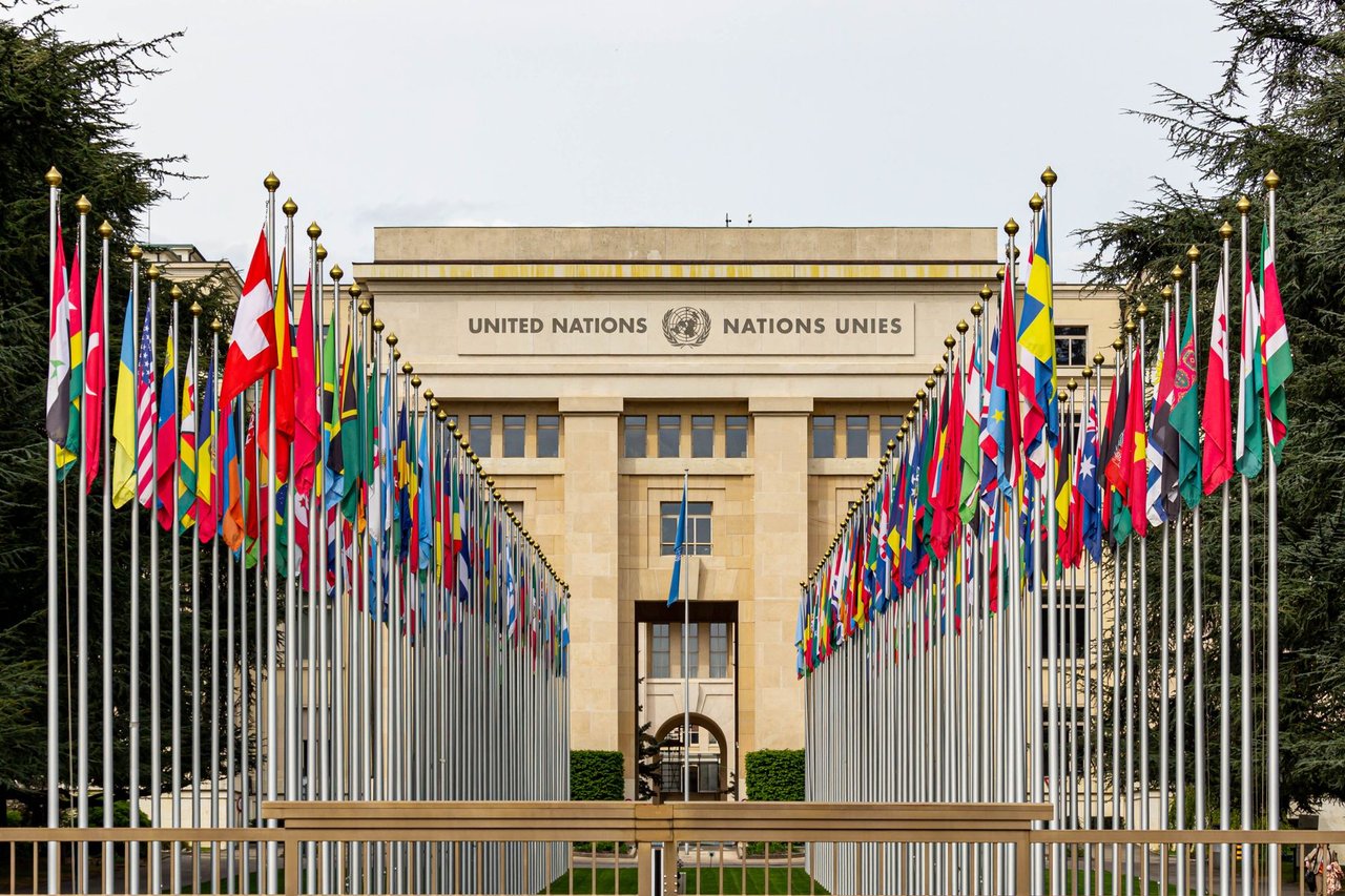 Edifício do escritório da ONU em Genebra cercado por bandeiras de diversos países.