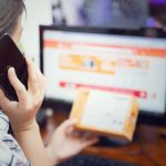 Mulher usa o celular enquanto confere uma encomenda de compra online em casa.
