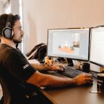 Profissional usando fones de ouvido e trabalhando em um computador com dois monitores em um escritório moderno.