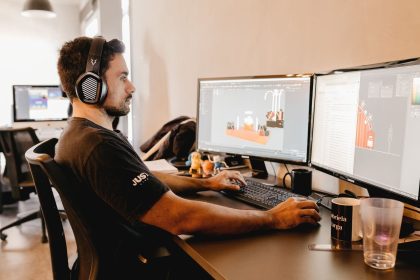 Profissional usando fones de ouvido e trabalhando em um computador com dois monitores em um escritório moderno.