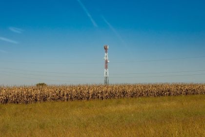 Torre de comunicação instalada em um campo rural sob céu azul.