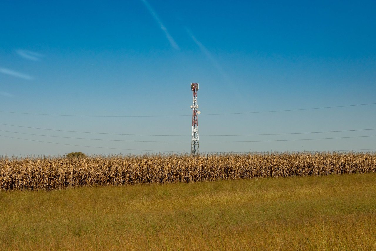 Torre de comunicação instalada em um campo rural sob céu azul.