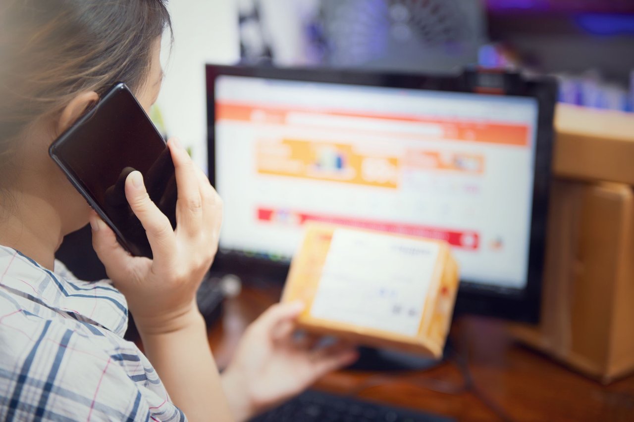 Mulher usa o celular enquanto confere uma encomenda de compra online em casa.