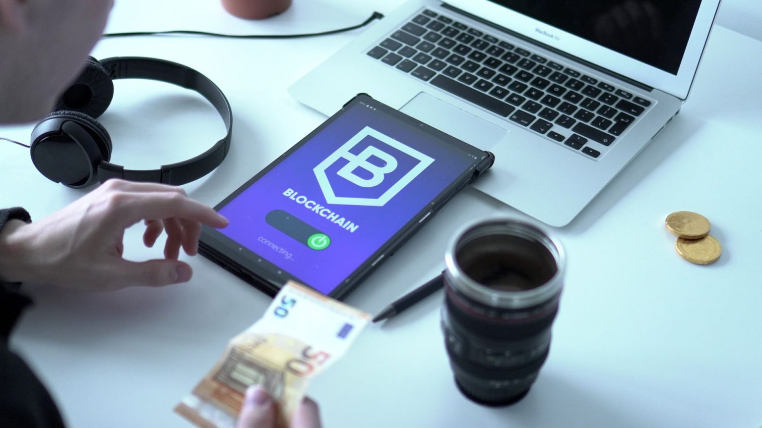 Tablet exibindo uma transação digital ao lado de um laptop e cédulas de euro.