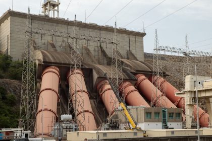 Usina hidrelétrica de grande porte com estruturas industriais e linhas de transmissão de energia.